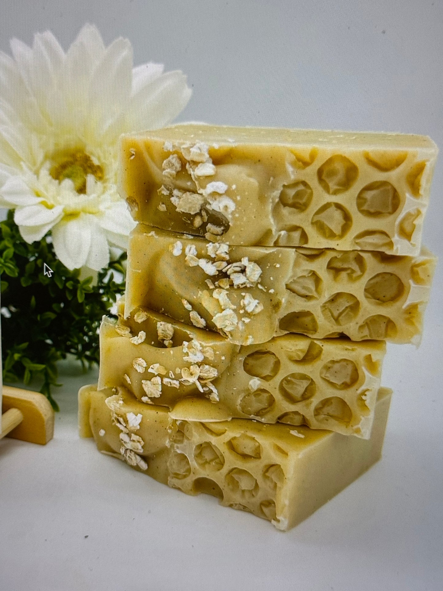 Stack of beige soap bars with a honeycomb pattern on top, garnished with flower petals, on a white background with a flower to the side.