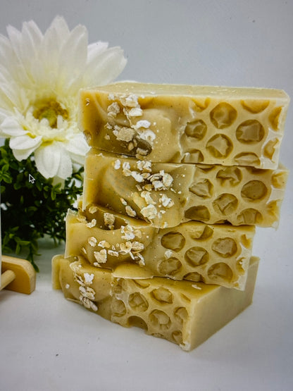 Stack of beige soap bars with a honeycomb pattern on top, garnished with flower petals, on a white background with a flower to the side.