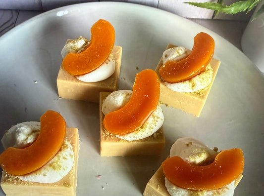 A wax melt with a peach cobbler scent, featuring a peach slice on top, placed on a white surface.