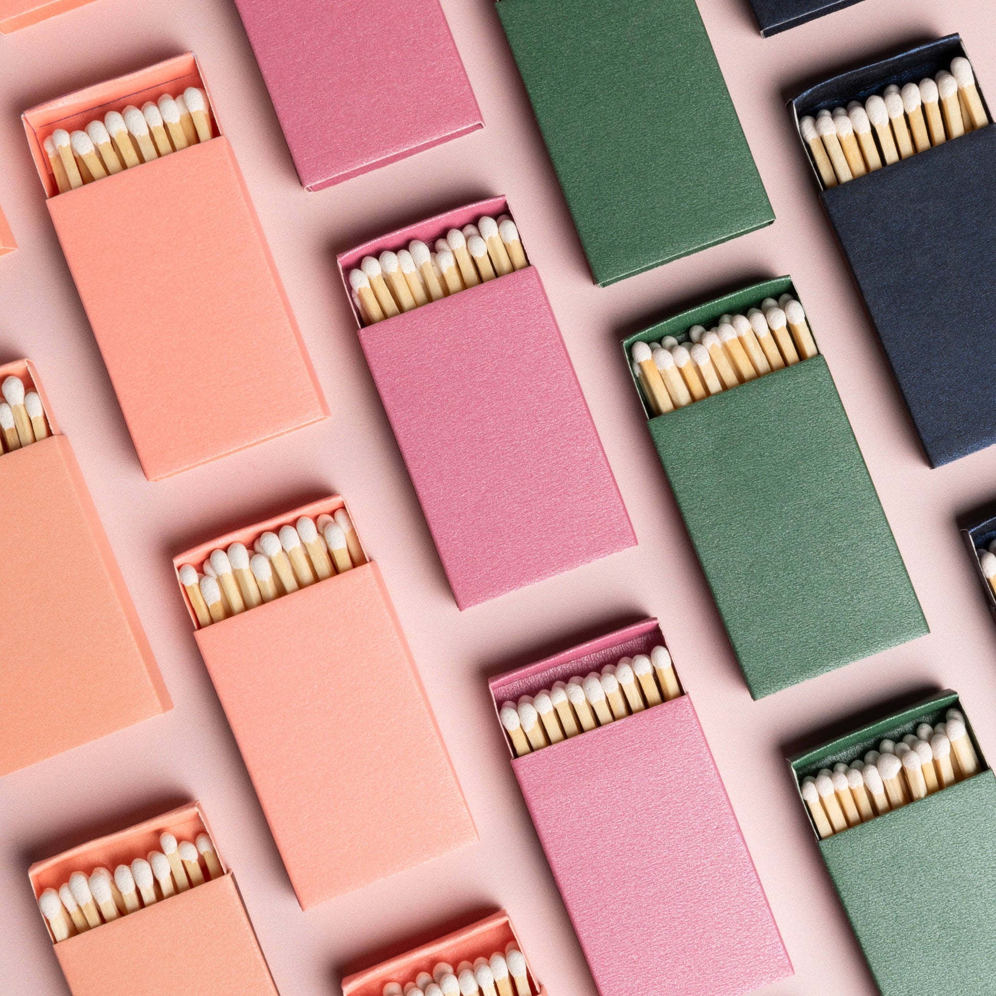 A collection of matchboxes in various colors including blue, pink, green, and orange, filled with white matchsticks, arranged neatly.