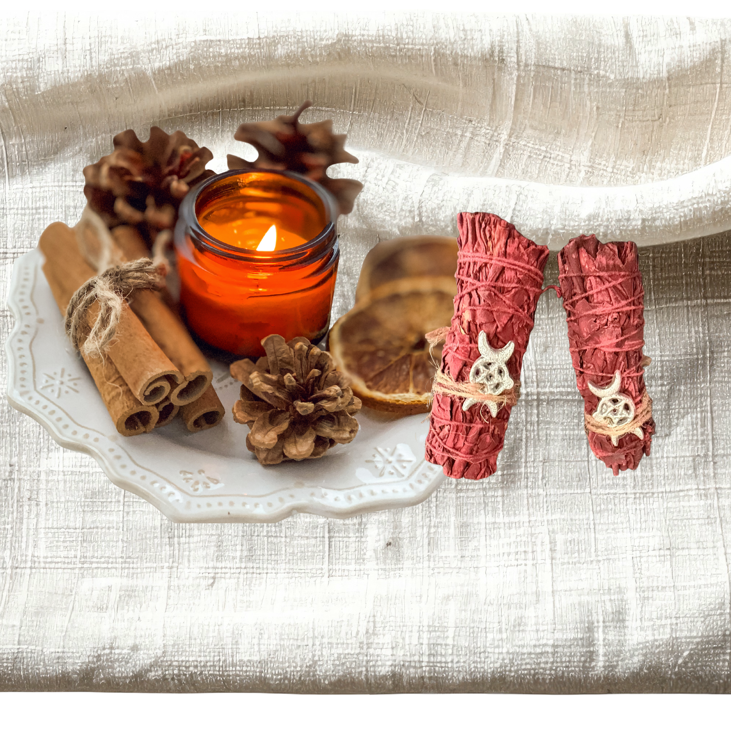 Candle with cinnamon sticks, pine cones, and smudge sticks on a textured surface